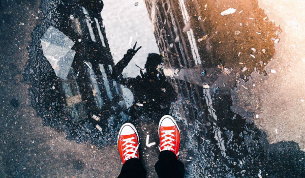 a photo of someone shooting his own reflection with a photocamera in a rainy puddle on the street.